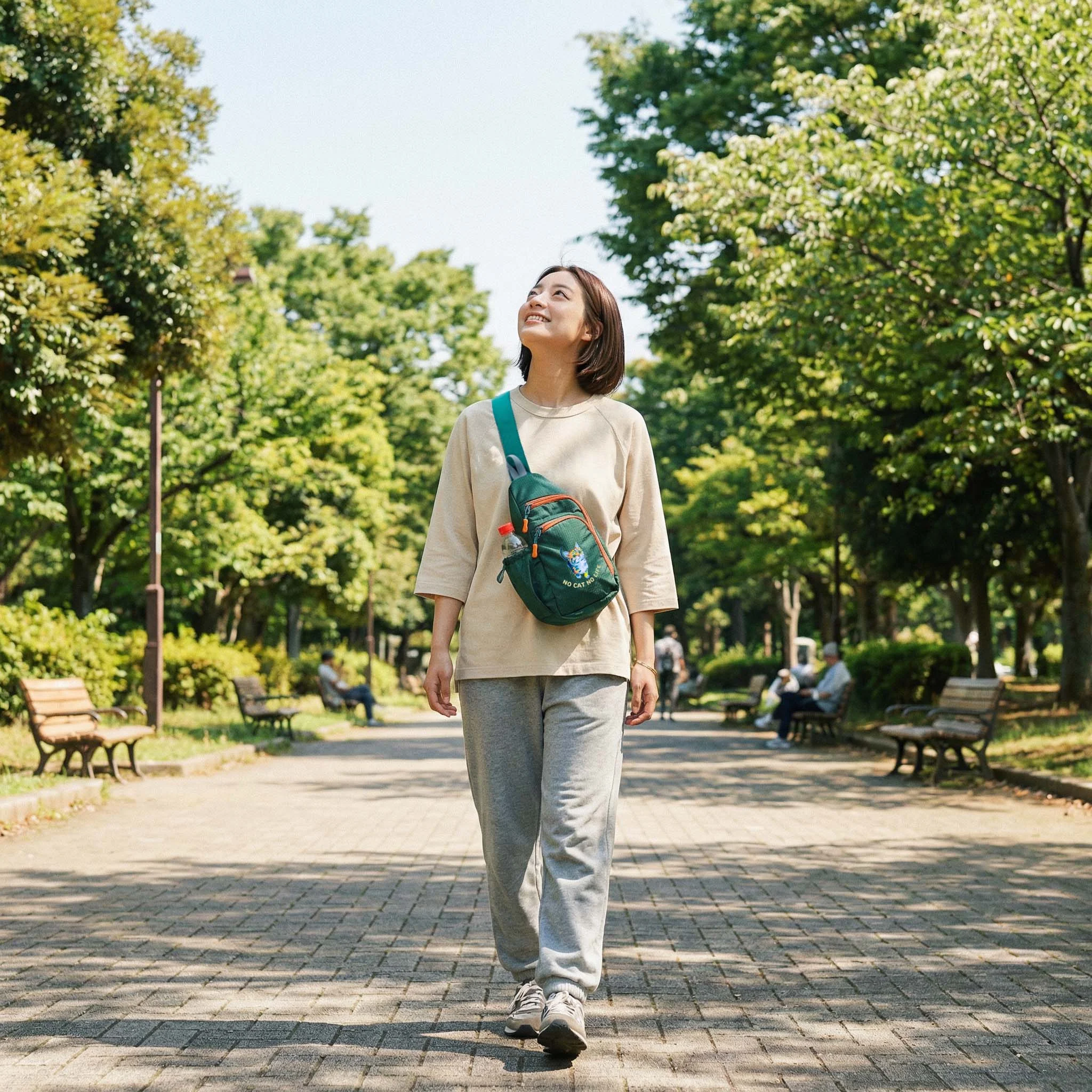 公園を歩く女性・グリーンのNEKONI SLINGバッグ