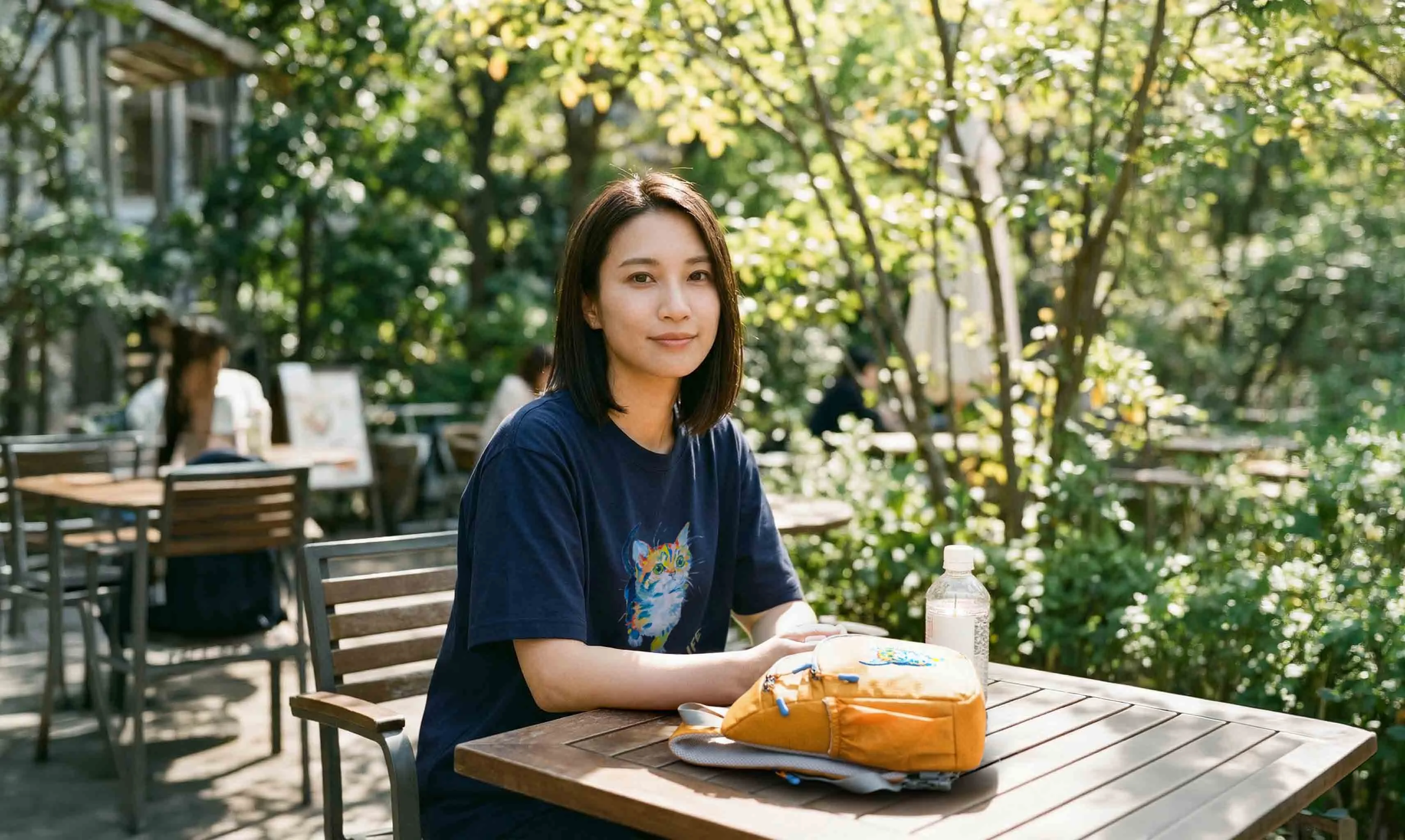 カフェテラスでくつろぐ女性・オレンジのNEKONI SLINGバッグ